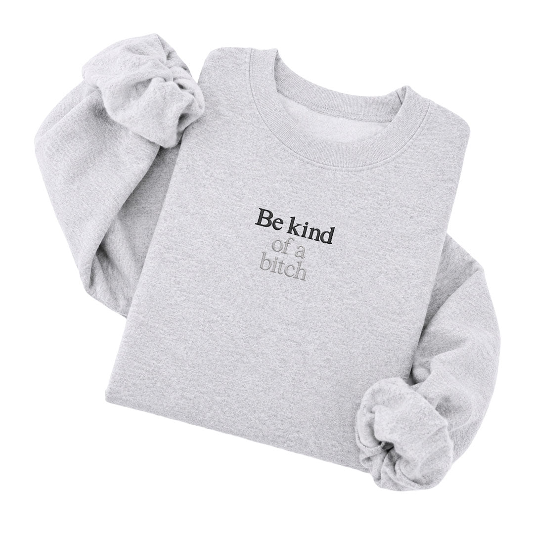 Ash crewneck sweatshirt embroidered with Be kind in black thread and of a bitch in tonal thread below