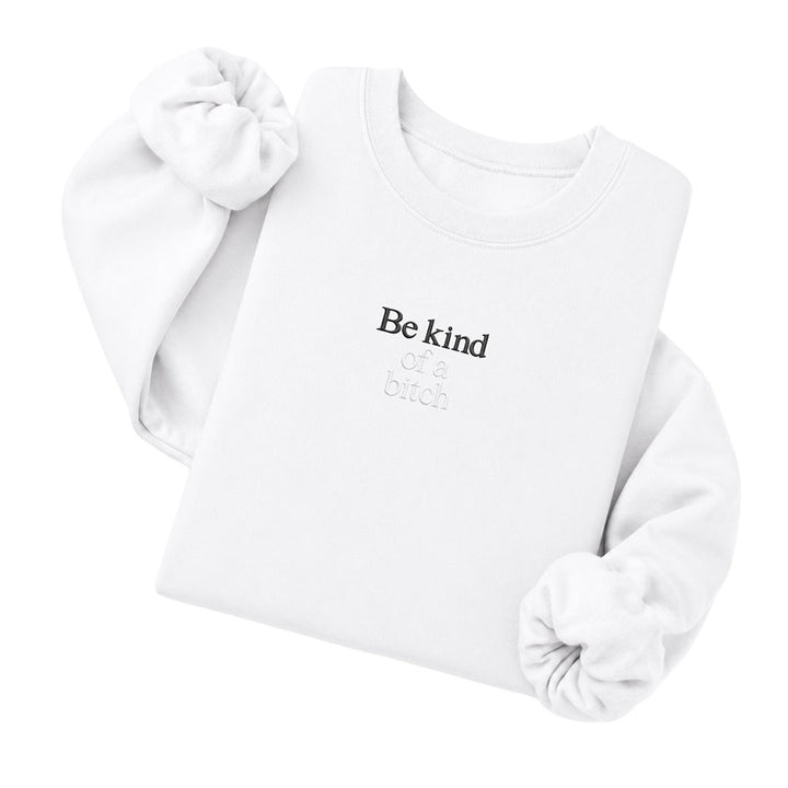 White crewneck sweatshirt embroidered with Be kind in black thread and of a bitch in tonal thread below