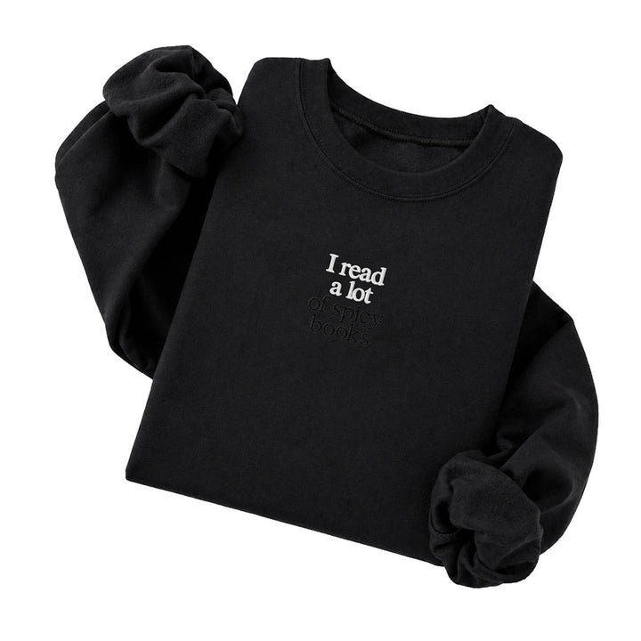 Black crewneck sweatshirt embroidered with I read a lot in white thread and of spicy books in tonal thread below