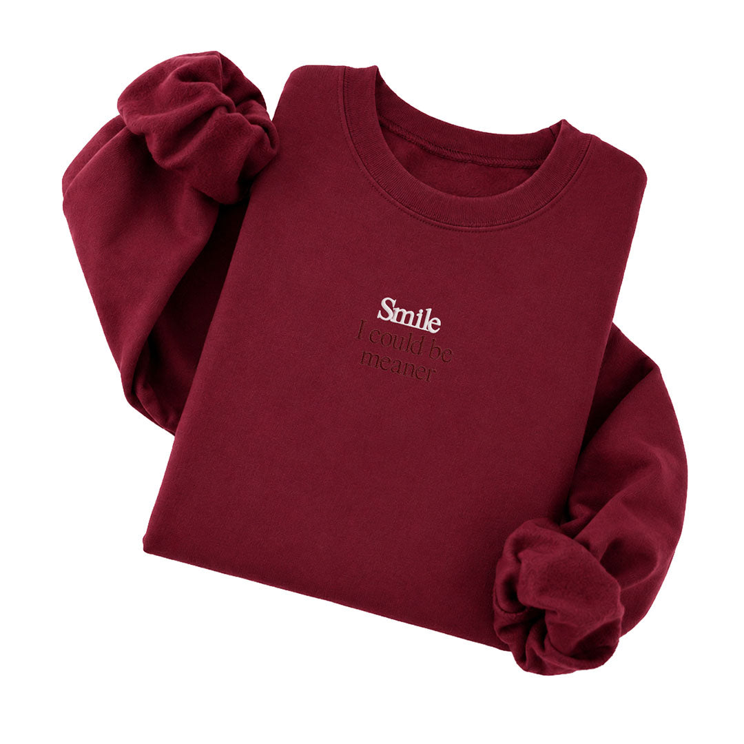 Garnet crewneck sweatshirt embroidered with Smile in white thread and I could be meaner in tonal thread below