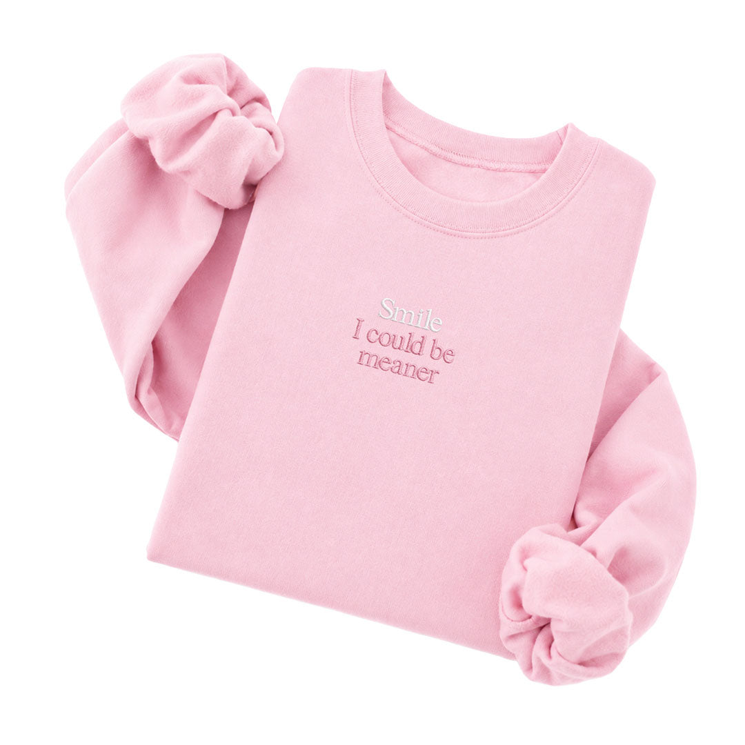Light Pink crewneck sweatshirt embroidered with Smile in white thread and I could be meaner in tonal thread below