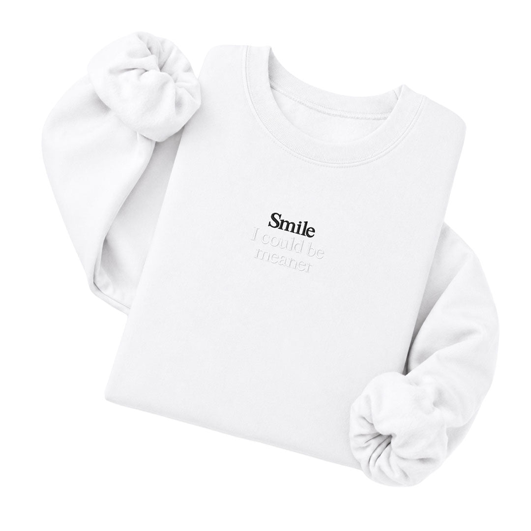 White crewneck sweatshirt embroidered with Smile in black thread and I could be meaner in tonal thread below